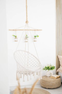 A cozy hanging chair surrounded by green plants in a bright, serene interior. clipart