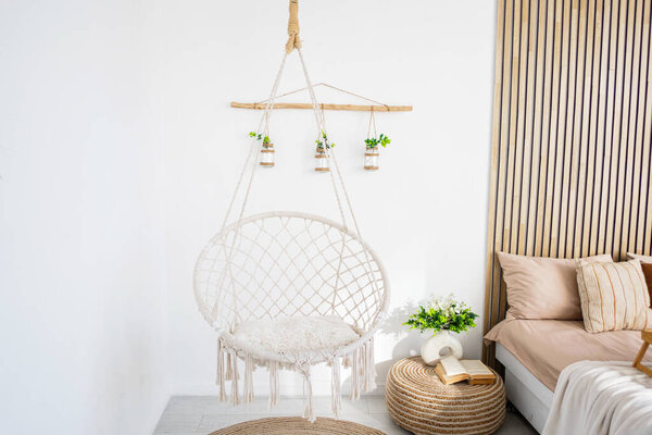Висячий стул придает очарование светлой комнате с мягкими постельными принадлежностями и растениями.