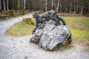Vaşağın detaylı bir heykeli orman yolu boyunca bir kayanın üzerinde duruyor..