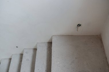 Tamamlanmamış merdiven açık bir alana açılıyor. Duvarda açık kablolar var..