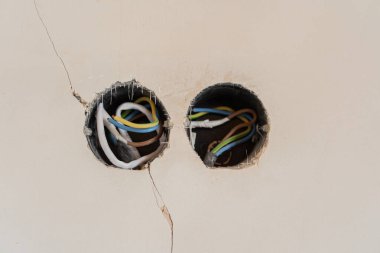 Açığa çıkan elektrik kabloları çatlak bir duvardaki deliklerden görülür..
