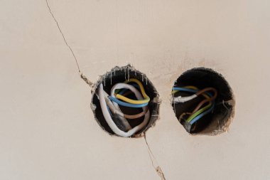 Two circular openings in a wall reveal exposed electrical wiring inside. clipart