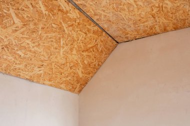 Geniş bir odada tadilat sırasında ahşap bir tavan ve tamamlanmamış duvarlar bulunur..