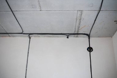 Çıplak bir odanın köşesindeki beton tavan boyunca uzanan siyah kablolar..