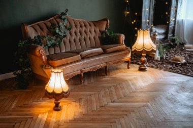 Zarif lambaları olan klasik bir kanepe, sıcak bir ortamda kapalı bitkilerle çevrili..