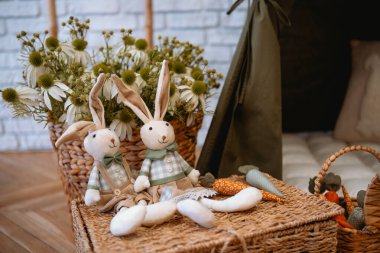 Süslü bir yaşam alanında renkli havuçların yanında iki pelüş tavşan oturuyor..