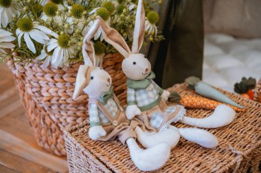 Çiçek ve yeşillik dolu bir sepetin yanında iki pelüş tavşan oturuyor..