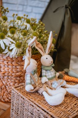 İki pelüş tavşan sıcak ve davetkar bir ortamda taze çiçeklerin arasında otururlar..