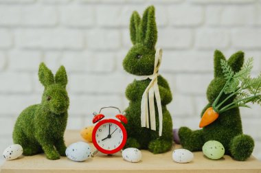 Üç yeşil tavşan süslemesi renkli yumurtalar ve antika bir saatin yanında durur..