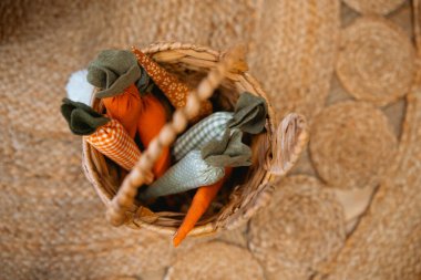 Colorful fabric carrots arranged in a wicker basket on a natural rug. clipart