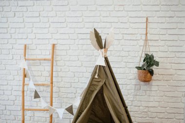 Bir çocuğun oyun alanında duvarın yanında asılı dekorlu küçük bir çadır vardır..