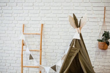 Oyun alanında dekoratif bayraklı bir çadır ve duvara dayalı tahta bir merdiven bulunur..