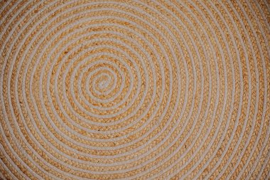 Woven mat features an elaborate spiral pattern with natural fibers in soft hues. clipart