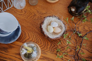 Brightly colored eggs are arranged in a nest on a wooden table with decor items. clipart