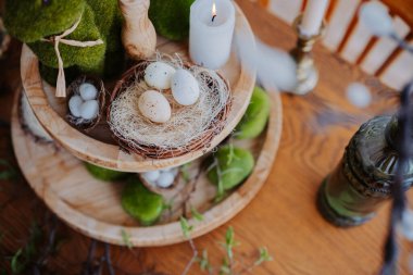 A spring-themed decoration features eggs in a nest with candles and greenery. clipart