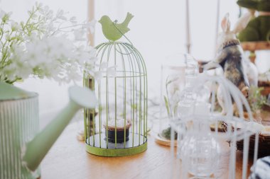 Green birdcage highlights a plant alongside gardening tools and decorations indoors. clipart