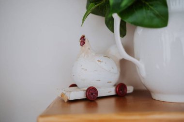 A wooden chicken on wheels sits on a shelf near a white ceramic pitcher. clipart