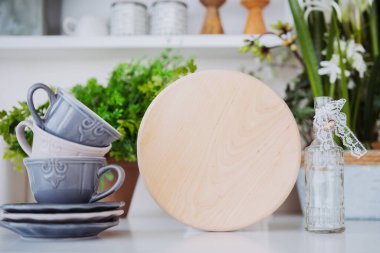 Three gray ceramic cups sit beside a round wooden display stand and a glass bottle. clipart