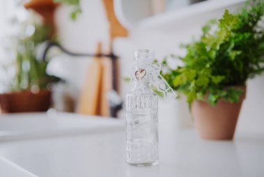 Small glass bottle decorated with lace and flowers sits on a kitchen countertop. clipart