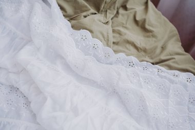 Beyaz dantel ve bej pamuk da dahil olmak üzere çeşitli kumaş dokuları yayılmış..