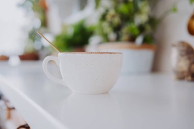 Ilık bir içecekle dolu beyaz bir bardak parlak bir tezgahın üzerinde duruyor..