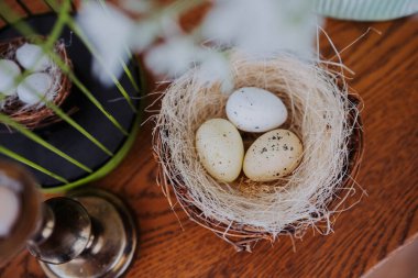 Tahta bir masada samanla dolu bir sepette üç güzel dekore edilmiş yumurta dinleniyor..