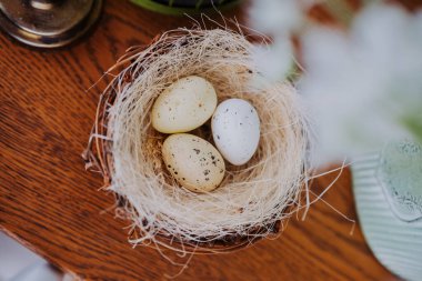 Üç pastel renkli yumurta, ahşap bir masanın üstündeki saman yuvasında dinleniyor..