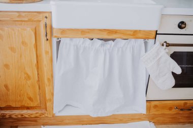 Büyüleyici bir mutfak beyaz bir perde ve ahşap bir dolap sergiler, rahat bir yer yaratır..