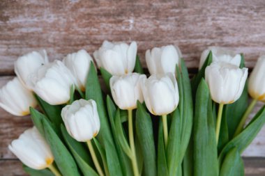 İçerideki ahşap yüzeyde yeşil yapraklı taze beyaz laleler sergileniyor..