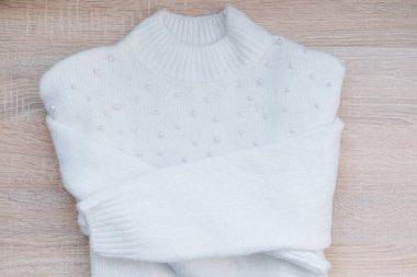 İnci süslemeli şık beyaz bir süveter ahşap bir yüzeyde duruyor..