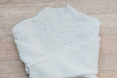 İnci süslemeli rahat beyaz bir süveter ahşap bir yüzeye güzelce katlanır..