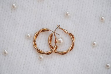 Twisted gold hoop earrings are displayed with pearls on soft fabric. clipart