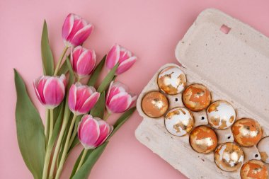 Pastel pembe arka planda laleleri olan bir karton kutuda paskalya yumurtası..