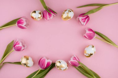 Pastel pembe arka planda laleleri olan Paskalya altın yumurtaları. Boşluğu kopyala. 