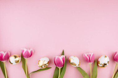 Pastel pembe arka planda laleleri olan Paskalya altın yumurtaları. Boşluğu kopyala. 