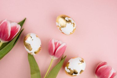 Pastel pembe arka planda laleleri olan Paskalya altın yumurtaları