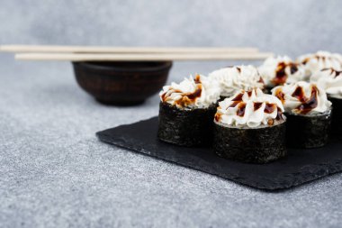 Üzerine krema ve sos konmuş suşi ruloları yemek çubuklarının yanındaki tabağa dizilmiş..