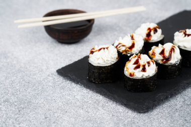 Suşi ruloları kremalı malzemeler ve desenli bir yüzeyde soya sosuyla kaplıdır..