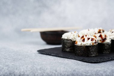 Taze hazırlanmış suşi ruloları ve kremalı soslar siyah bir tabakta sunuluyor..