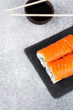 Soya soslu, koyu taştan bir tabakta sunulan taze somon suşisi ruloları..