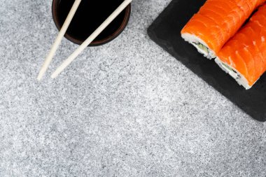 Renkli suşi ruloları ve soya sosu ile gri taşta yemek çubukları..