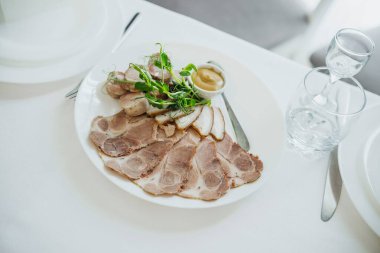 Dilimlenmiş etler taze yeşillik ve bir tabakta hardal ile sunulur..