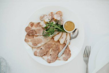 Dilimlenmiş et, karides ve beyaz bir tabakta küçük bir kase sos..