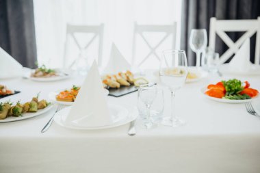 Yemek masası çeşitli tabaklar ve bardaklarla aydınlık bir ortamda düzenlenir..