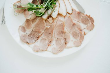 Dilimlenmiş etler, beyaz bir tabakta düzgünce dizilmiş, otlar taze bir dokunuş ekliyor..