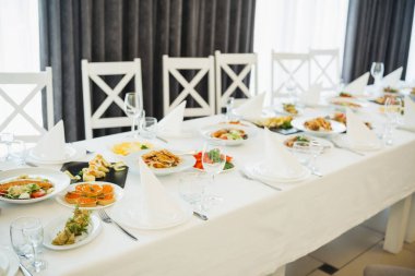 Güzel düzenlenmiş bir yemek masasında konuklar için çeşitli yemekler ve cam eşyalar sunulur..