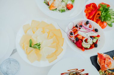 Renkli salata ve çeşitli peynirler açık hava ortamında beyaz bir masada sergilenir..