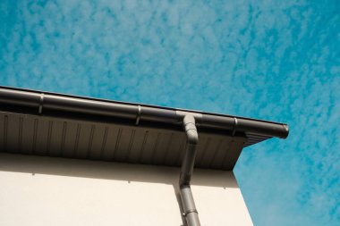 Bir çatı çizgisi mavi gökyüzü ile kesişiyor, modern mimari ve dokuları sergiliyor..