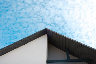 Bir bina köşesi, üzerinde tüylü beyaz bulutlar olan canlı bir mavi gökyüzü ile karşılaşıyor..