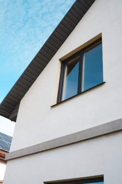Modern bir evde açık mavi gökyüzünün altında belirgin bir pencere bulunur..